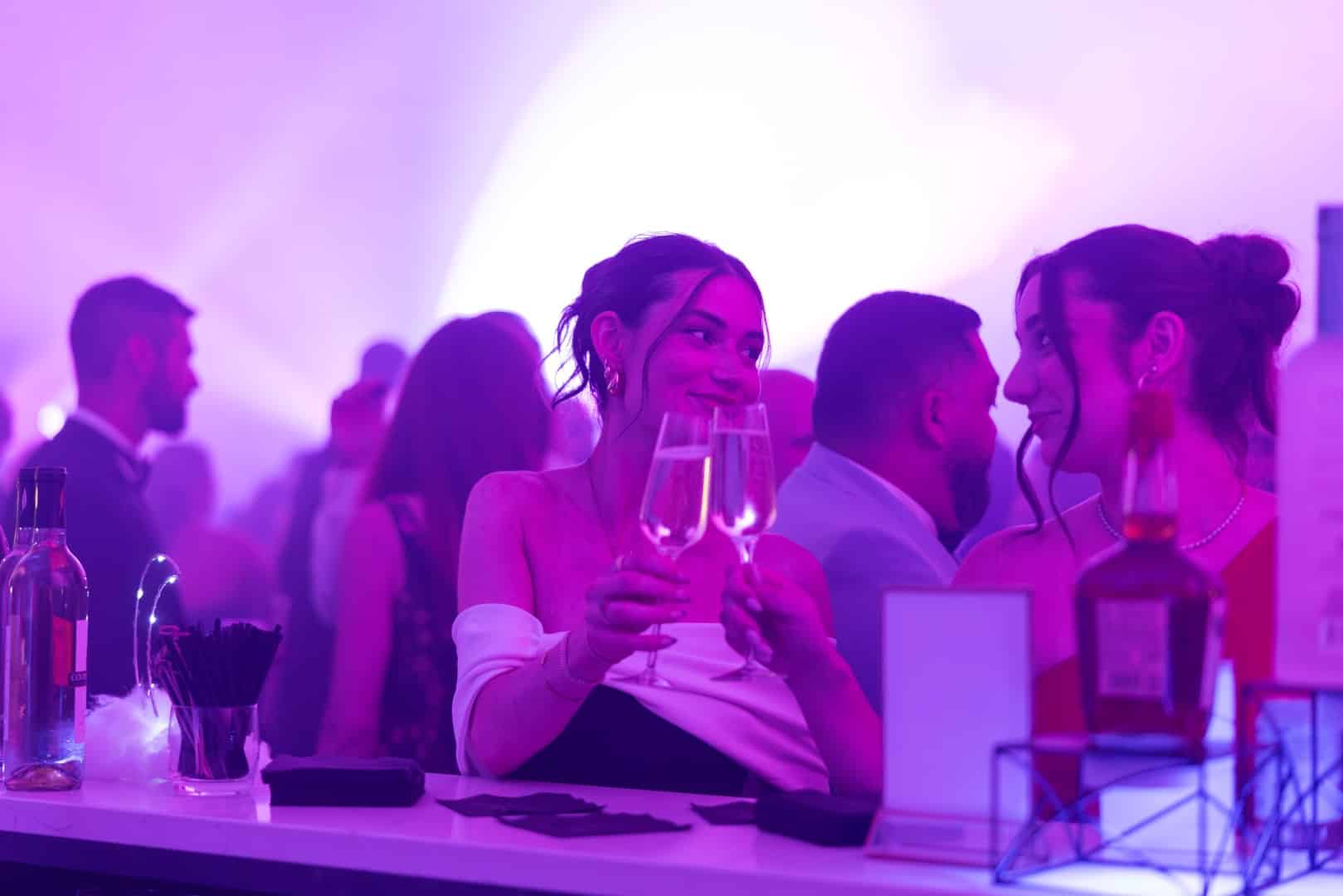 two guests clinking champagne glasses together at the Wishmaker's Ball after party.