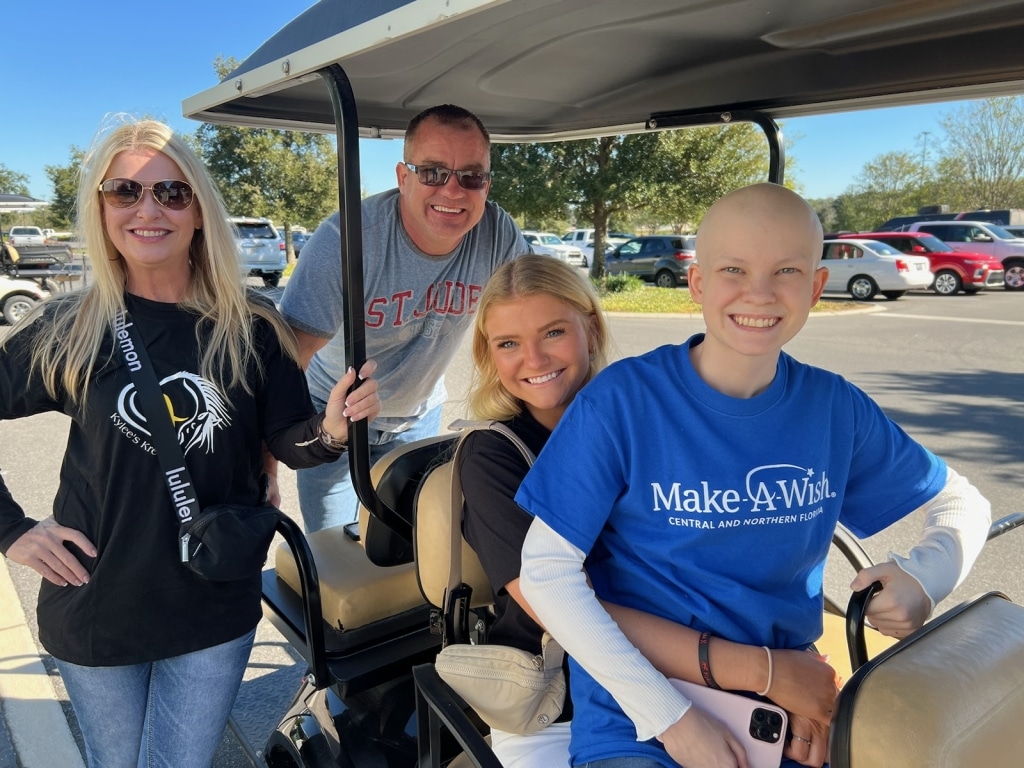 Wish kid Kylee in Make-A-Wish shirt surrounded by her family